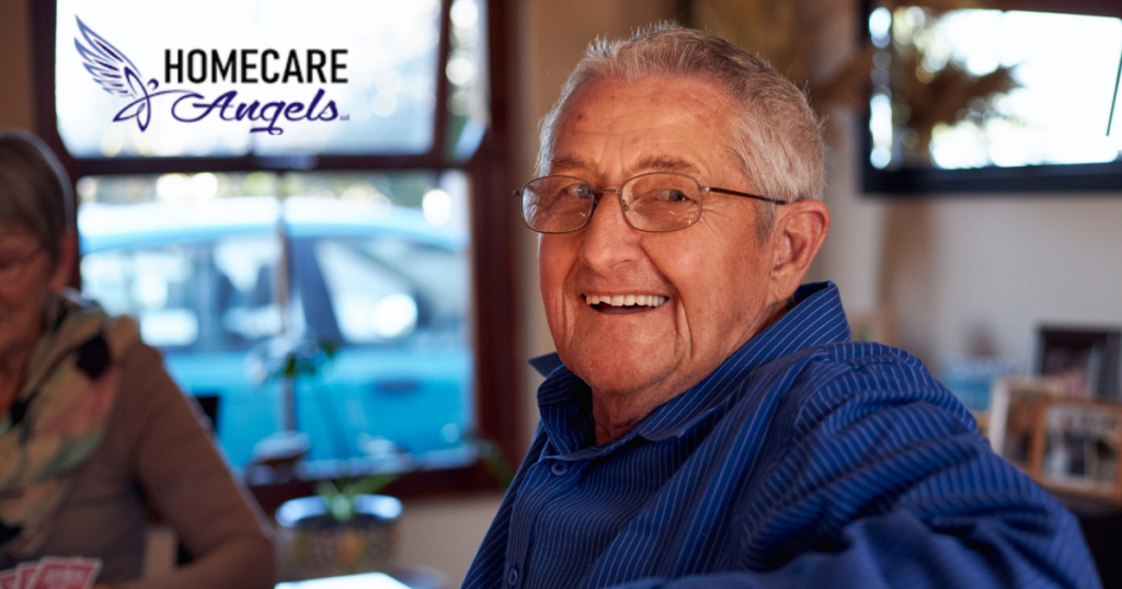 Smiling senior man sitting at a table, happy as a result of successful long-distance caregiving.