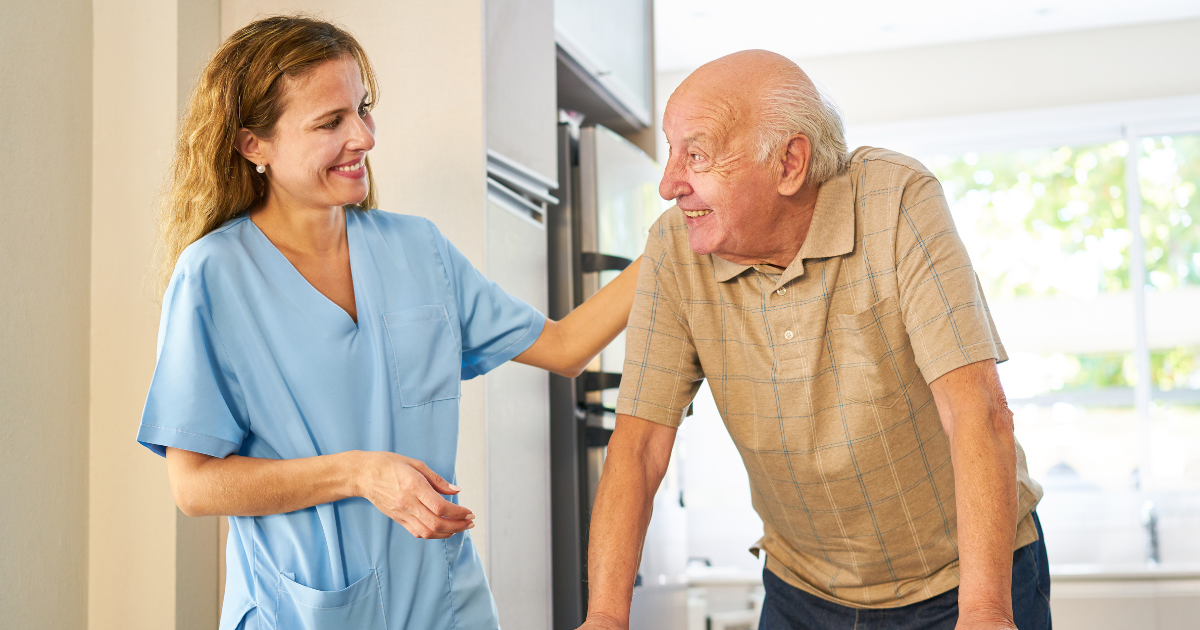 Caregiver smiling at senior man using a walker while providing ambulation assistance, a senior home care service.