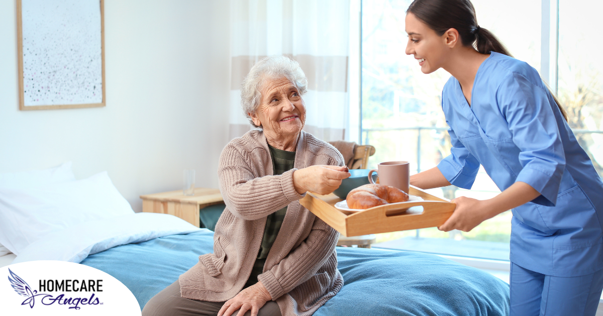 A professional caregiver smiles and provides food to an older adult in her care, representing the compassionate care needed for those with dementia.