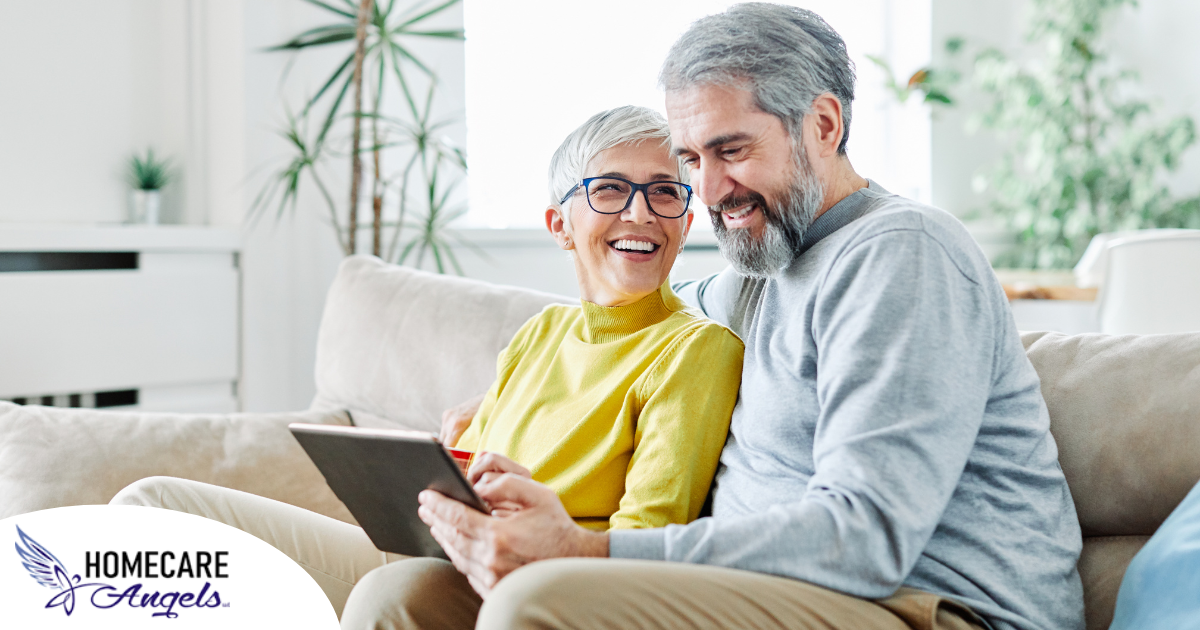 A senior couple smiles while looking at a laptop, showing how online resources can help family caregivers.