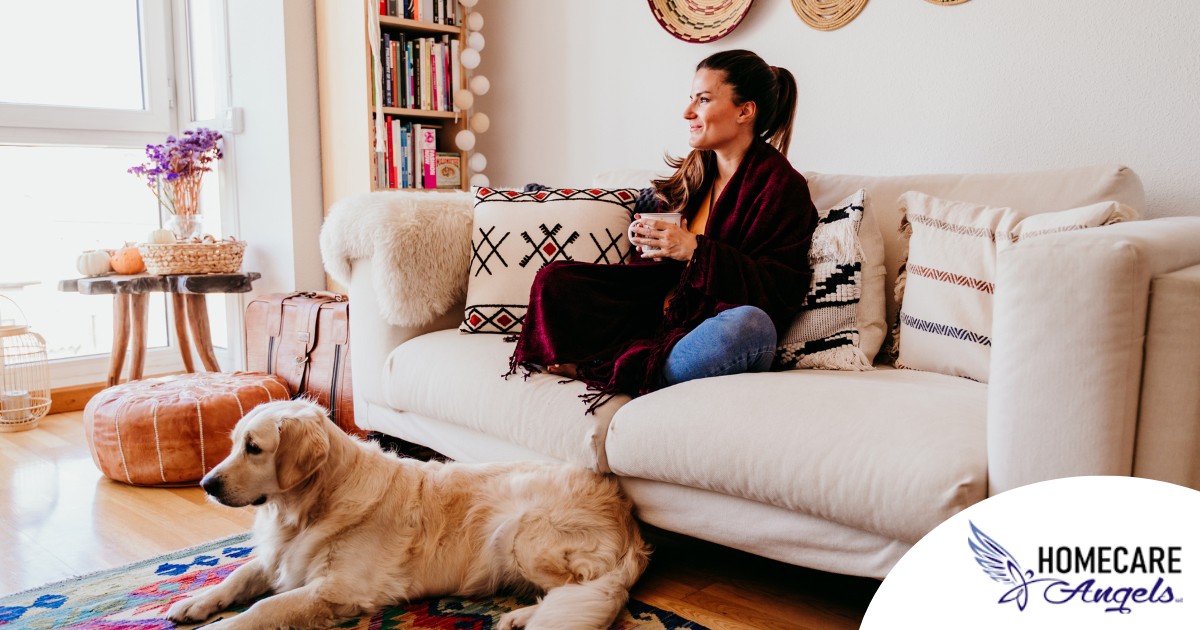 A woman relaxes with her dog while sipping on tea, representing how self-care can combat caregiver stress.