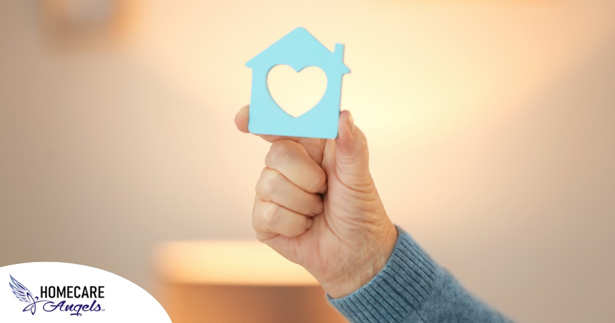 A hand holds up a cutout of a home with a heart in it, representing the home care industry.